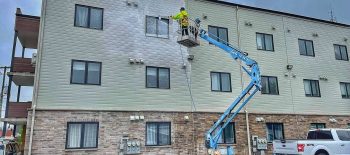 Workers painting a large mural on a building's exterior wall using a lift.